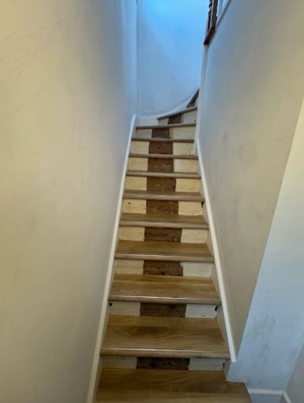 Narrow wooden staircase with alternating dark and light risers.