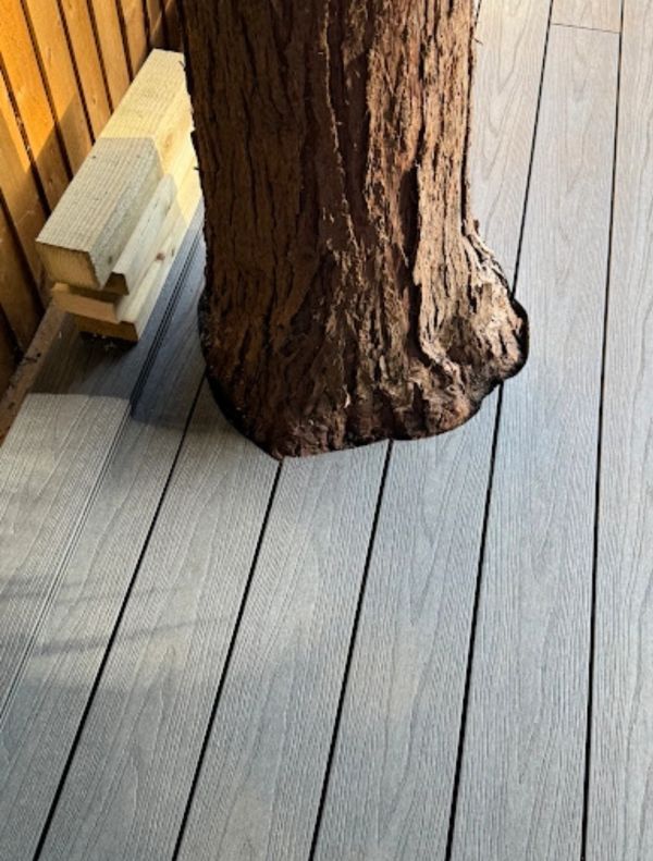 Tree trunk growing through a wooden deck with stacked lumber nearby.