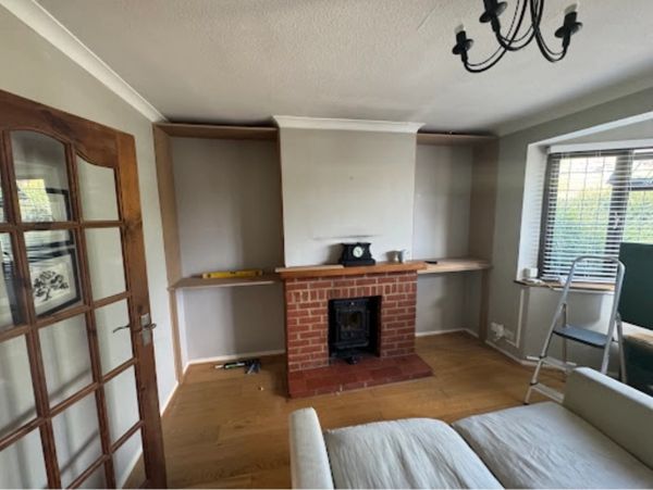 Living room with a brick fireplace and wooden shelves under construction.