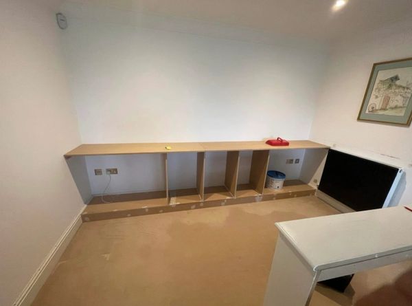 A partially assembled wooden shelf unit against a white wall in a room.
