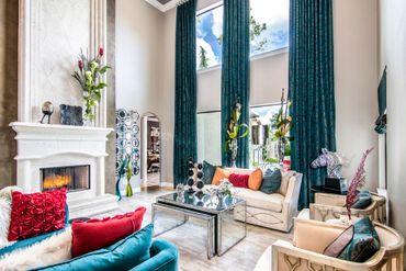 Elegant living room with high windows, vibrant cushions, and modern decor.