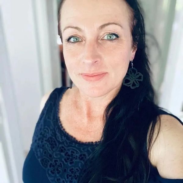 Woman with green eyes wearing a dark top and flower-shaped earrings.