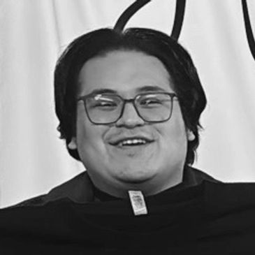 Smiling man with glasses and medium-length hair in black and white photo.