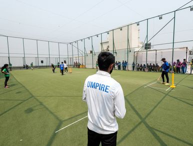 An umpire overseeing a cricket match on an outdoor field with players and spectators.