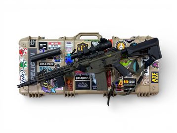 A tactical rifle resting on a sticker-covered hard case.
