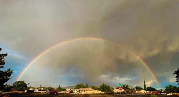 Full rainbow over a neighborhood with cloudy sky.