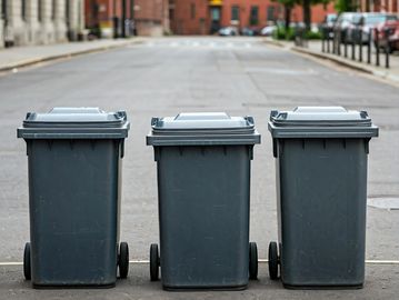 3 trash bins on a sidewalk in a city,