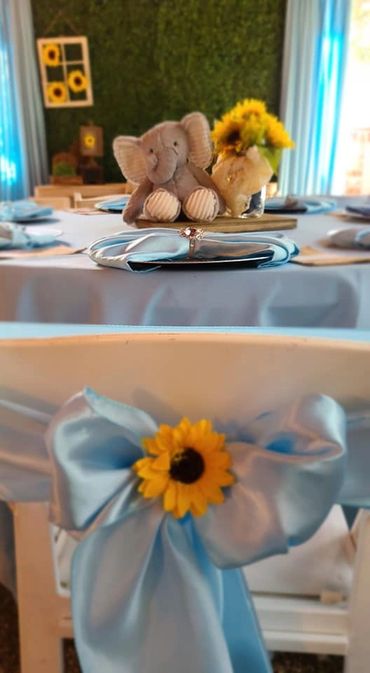 Soft elephant centerpiece and sunflower-themed table decor with blue ribbons.