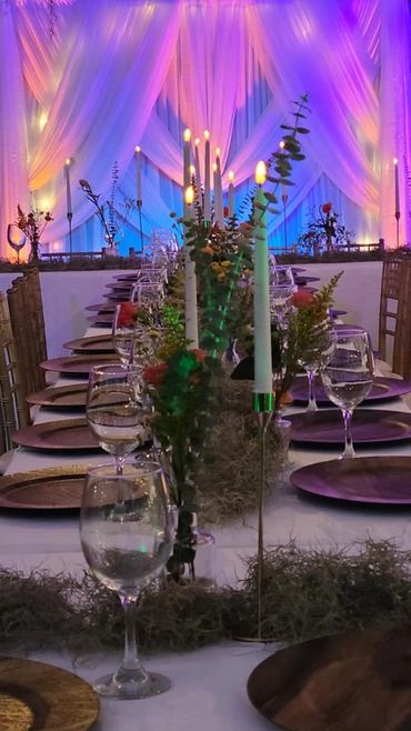 Elegant long dining table with candles and floral decorations under colorful drapes.