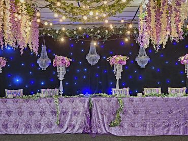 Elegant floral and crystal wedding table setup with purple theme and fairy lights.