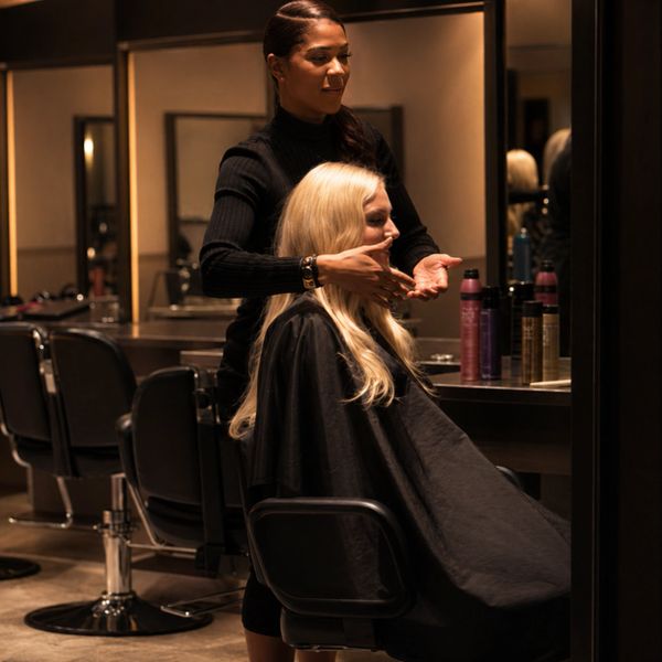 Hairdresser styling a seated woman's blonde hair in a salon.