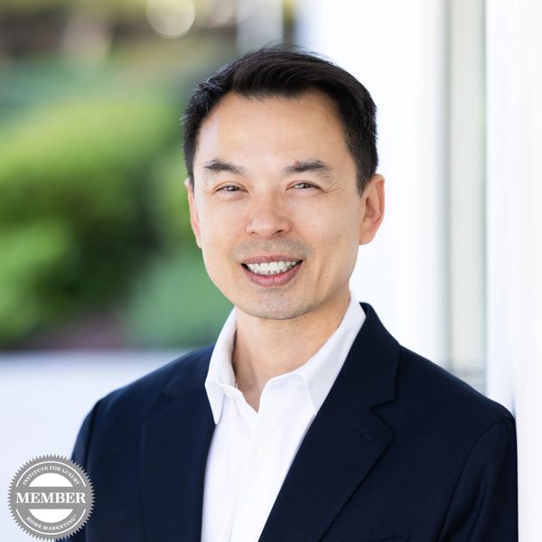 Professional man in suit smiling outdoors with blurred greenery background.