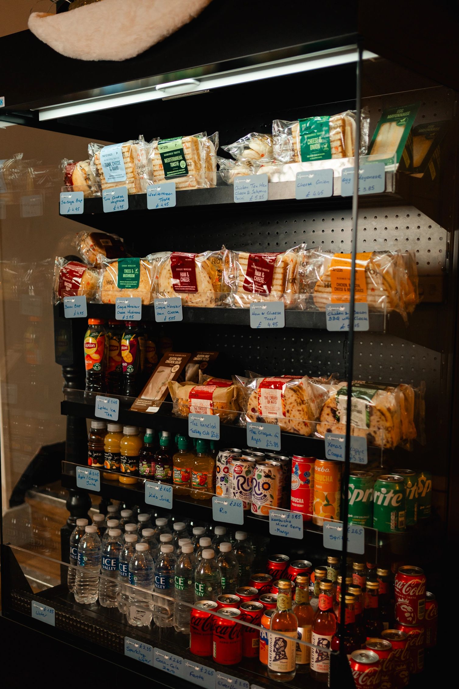 Refrigerated shelves stocked with sandwiches, juices, and sodas in a convenience store.