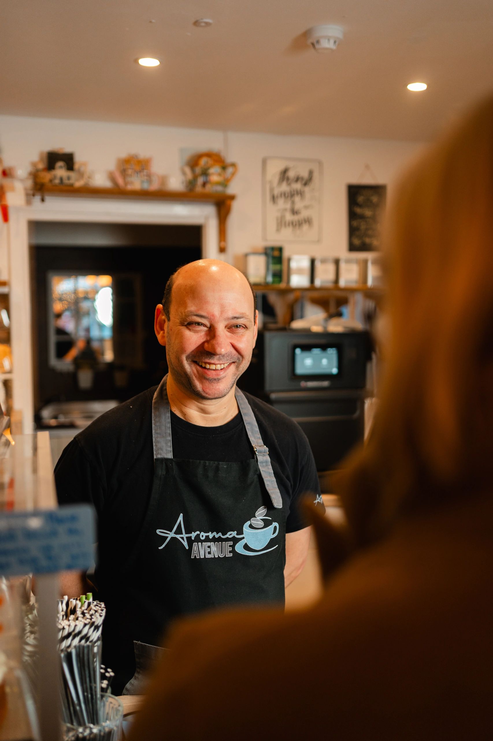Smiling barista in a coffee shop wearing an Aroma Avenue apron.