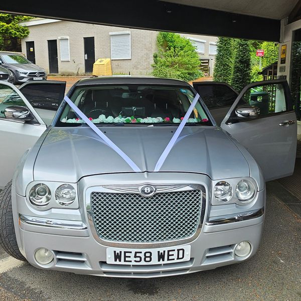 Silver car decorated with white ribbons and flowers, parked with doors open.