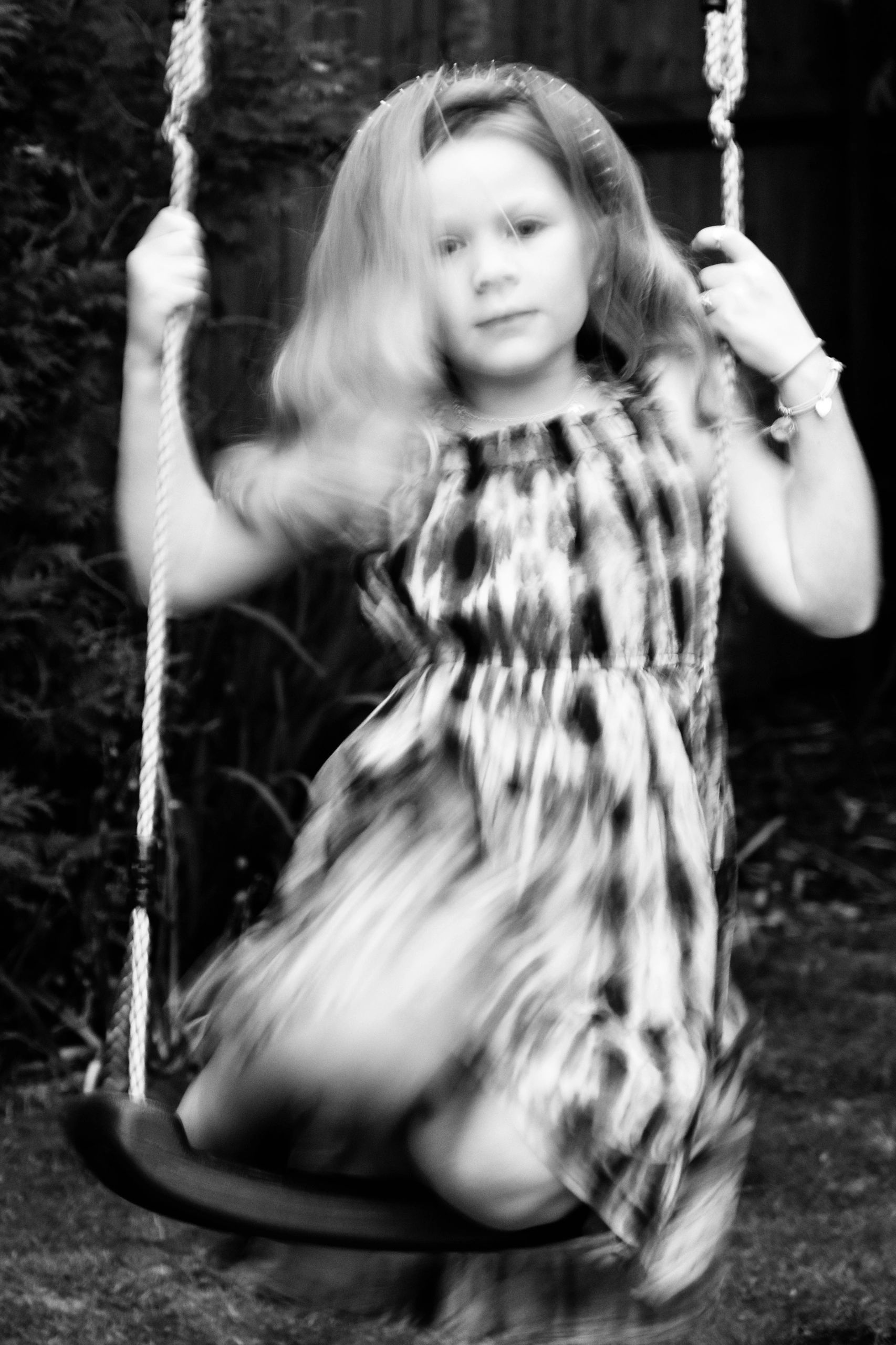 A young girl sits on a swing with whooshing dress.