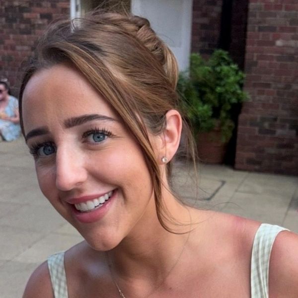 Young woman smiling outdoors with hair tied back.