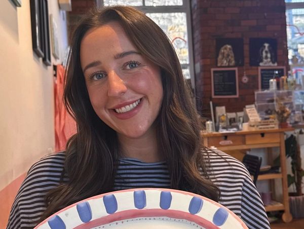 Smiling woman holding a colorful plate in a cozy cafe.