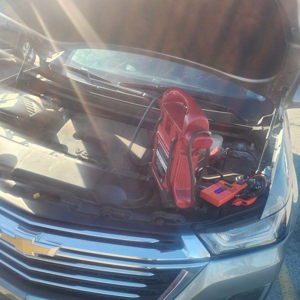 Car hood open with a red jump starter connected to the engine.