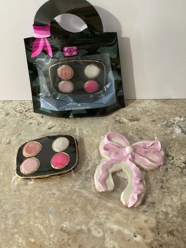 Decorative cookies shaped like a makeup palette and a pink bow on a countertop.