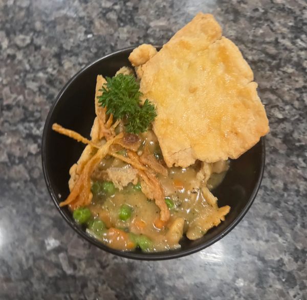 A bowl of vegetable pot pie with peas, carrots, crispy onions, and a golden crust.
