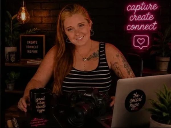 Woman smiling in a cozy creative workspace with neon signs and camera gear.