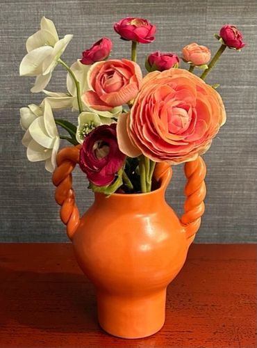 Orange vase with vibrant flowers on a wooden surface.