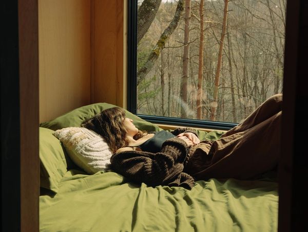 A woman resting on a bed with a green blanket looking out the window
