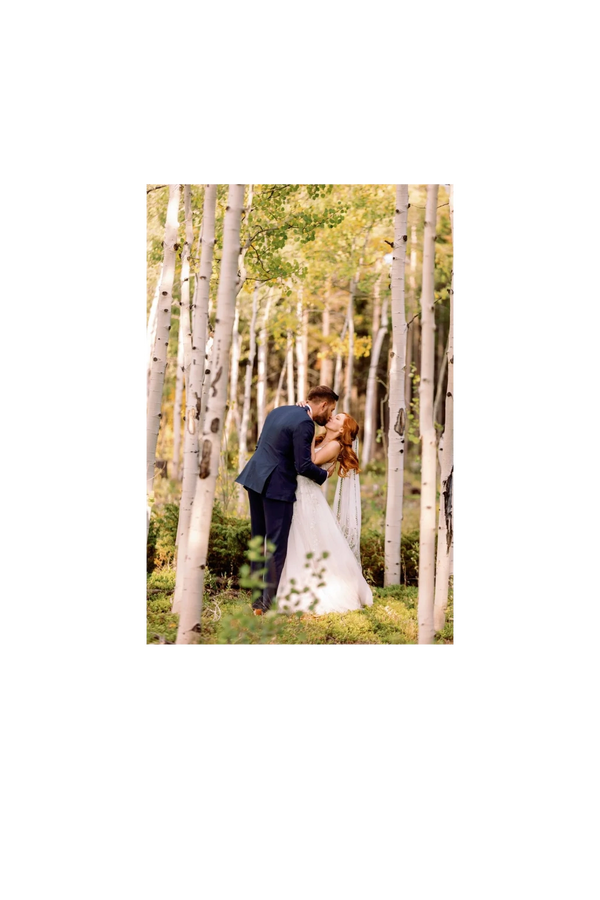 A newlywed couple shares a kiss in a serene birch forest.