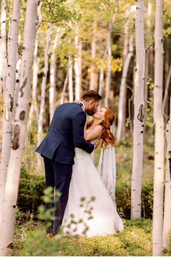 A newlywed couple shares a kiss in a serene birch forest.
