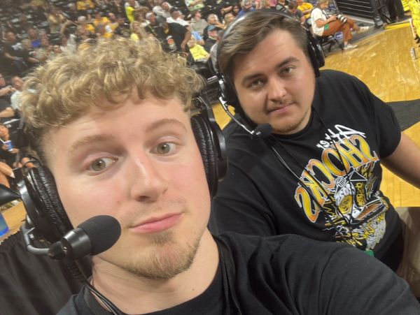 Two young men with headsets at a sports event, taking a selfie.