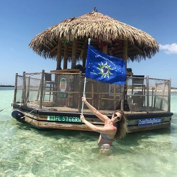 Woman in water holding a flag near a tiki hut float.