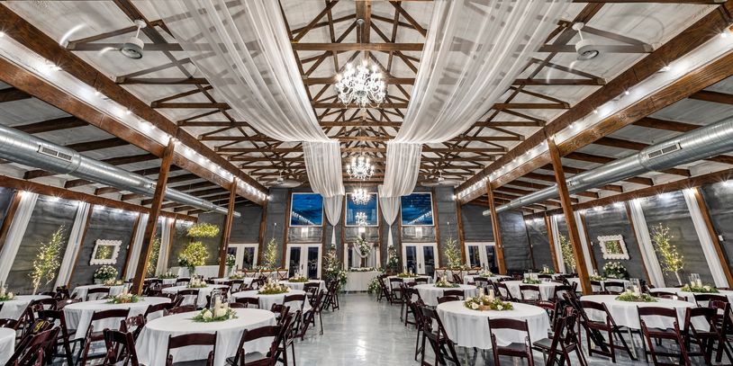 Elegant event hall with decorated round tables and chandeliers.