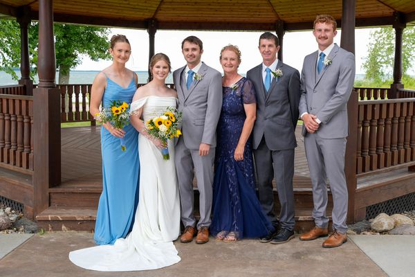 A wedding party poses in front of a wooden gazebo with sunflowers and elegant attire.