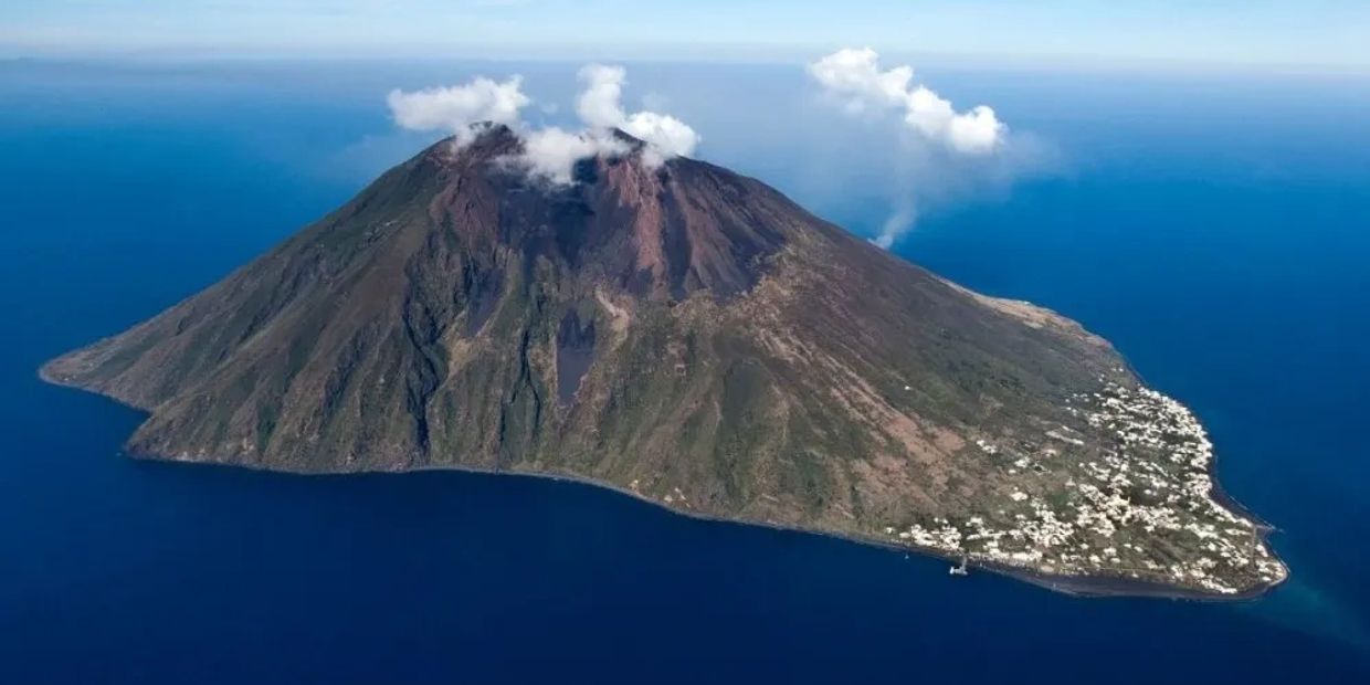 A volcanic island emitting smoke with a settlement on one side.