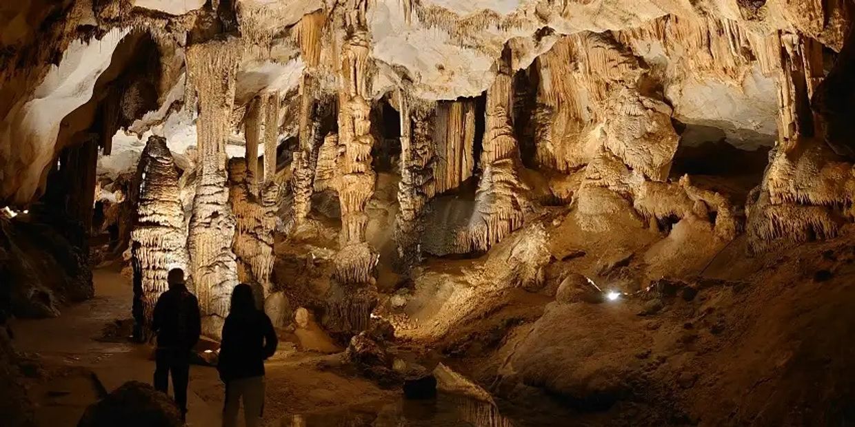 Two people explore an illuminated cave filled with stalactites and stalagmites.