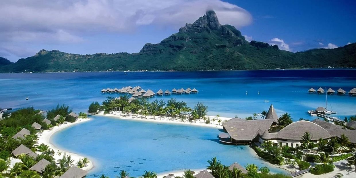 Tropical island resort with overwater bungalows and a mountain backdrop.