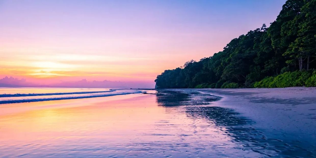 Calm beach at sunset with vibrant pink and purple sky reflecting on wet sand.