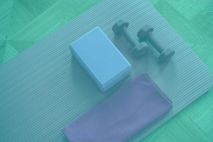 Yoga mat with block, dumbbells, and towel on wooden floor.