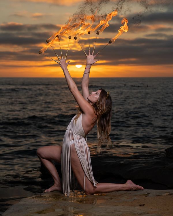 Woman on seaside cliff with fire finger flow props during sunset. Portrait photography, flow artist.
