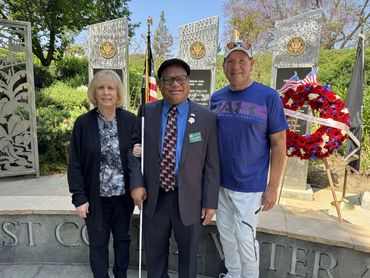 Ollie stands between a blonde woman in a black pant suit and floral shirt and a man in a white baseb