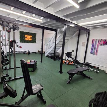 Modern home gym with various workout equipment and green flooring.