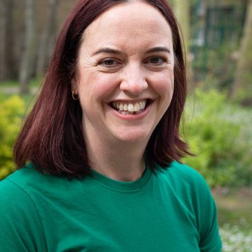Smiling woman with red hair wearing a green shirt outdoors.