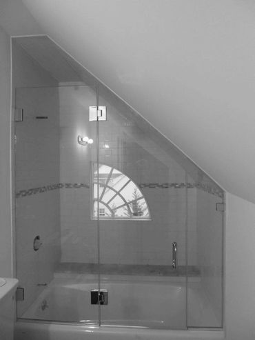 Bathroom with a glass shower enclosure under a slanted ceiling and a decorative window.