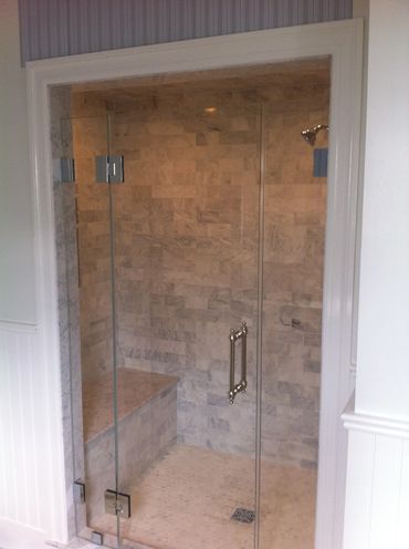 Elegant marble-tiled walk-in shower with glass door and built-in bench.