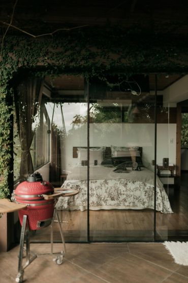 Cozy bedroom with floral bedding behind glass doors and a red grill outside.