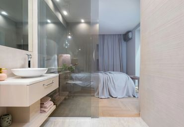 Modern bathroom with glass partition revealing a cozy bedroom.