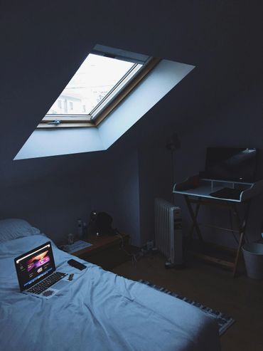 Cozy bedroom with skylight, laptop on bed, and minimalistic desk setup.