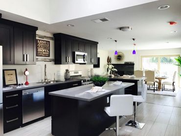 Modern kitchen with black cabinets, white countertops, and a dining area with natural light.