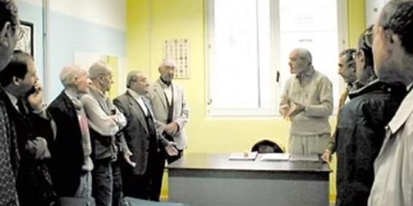 Elderly men attentively listening to a speaker in a bright room.